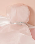 Ava silver-tone open bangle with overlapping rows of clear stones, displayed around blush fabric.