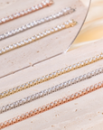 Diana tennis bracelets with round clear stones in three metal tones, displayed on pale stone beside a mirror.