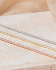 Quinn tennis bracelets with clear stones in silver, yellow-gold and rose-gold tones on pale stone.